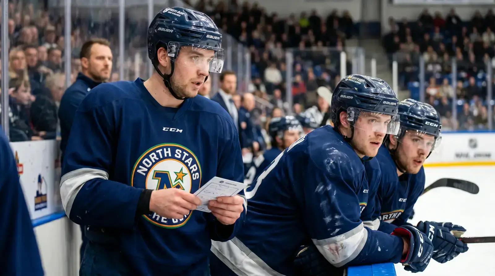Newly acquired NHL player sitting on the bench studying the playbook with teammates
